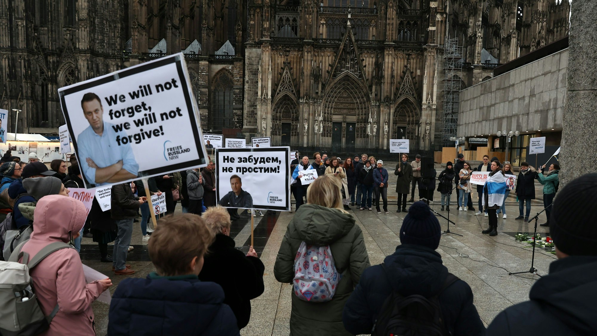 Menschen mit Plakaten stehen in Köln auf der Domplatte.