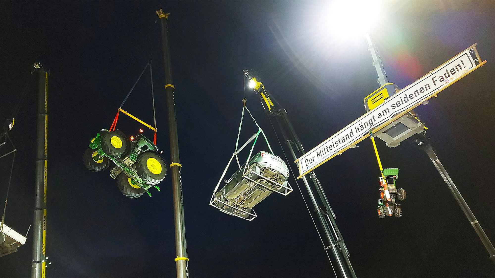 Traktoren, ein Pritschenwagen und ein Pkw schwebten während einer Kundgebung an Kranauslegern.