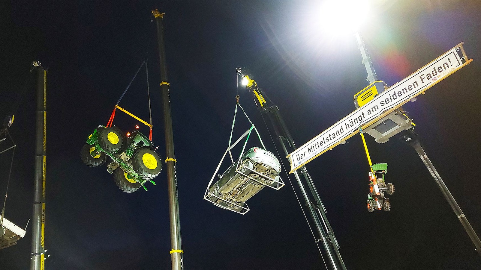 Traktoren, ein Pritschenwagen und ein Pkw schwebten während einer Kundgebung an Kranauslegern.