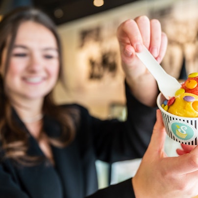 Die Besitzerin eines Eiscafés hält einen Becher mit zwei Kugeln Fruchteis. (Symbolbild)