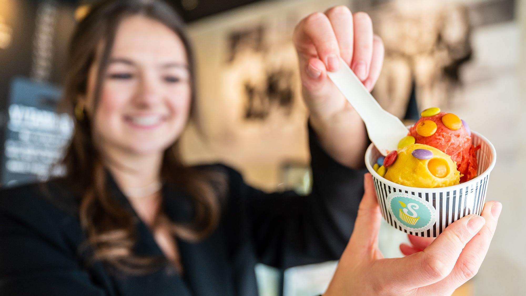 Die Besitzerin eines Eiscafés hält einen Becher mit zwei Kugeln Fruchteis. (Symbolbild)