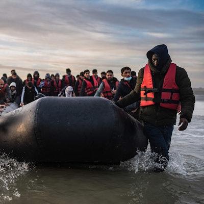 Migranten ziehen ein Schlauchboot aus dem Wasser am Strand von Gravelines.