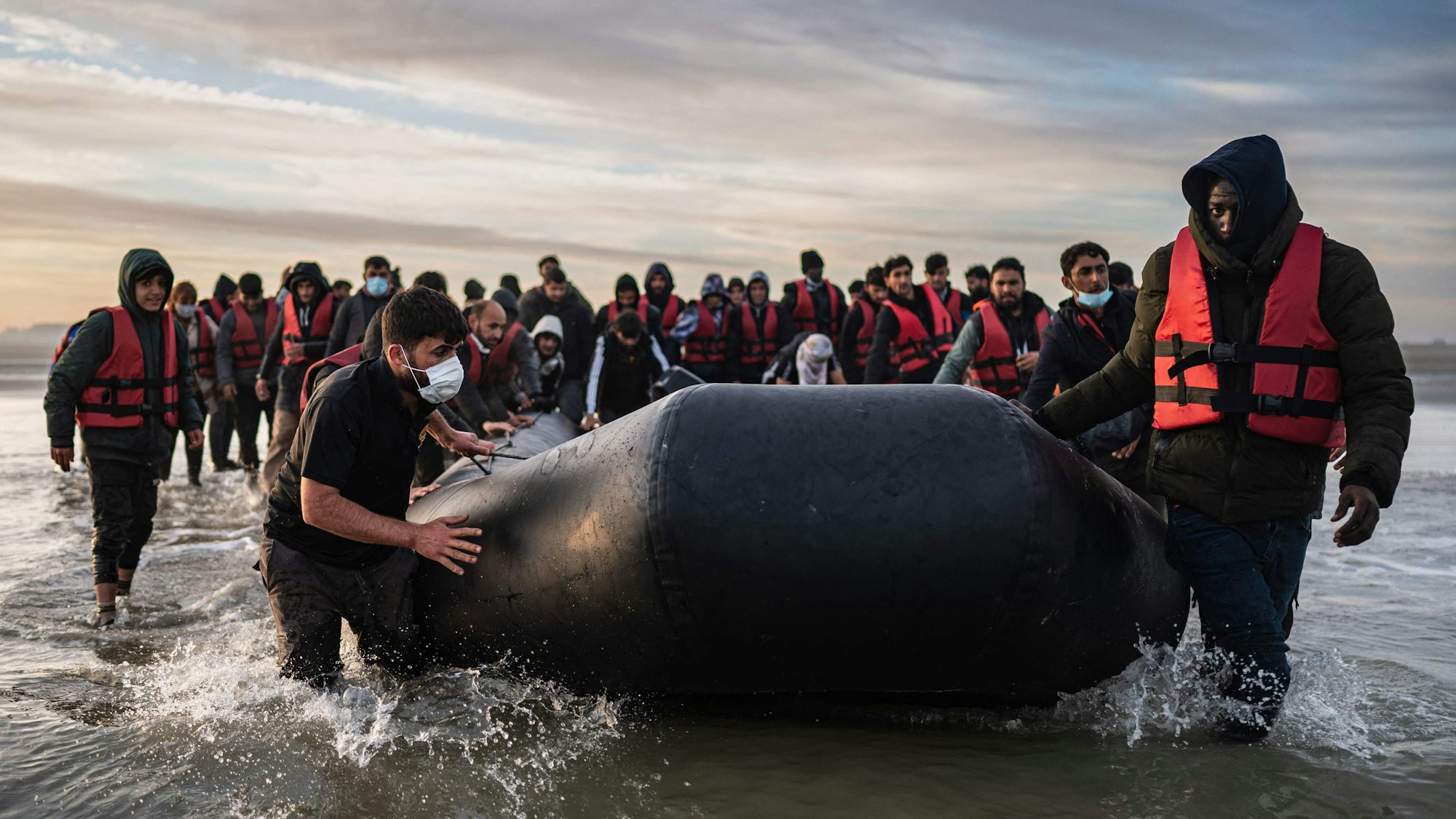 Migranten ziehen ein Schlauchboot aus dem Wasser am Strand von Gravelines.