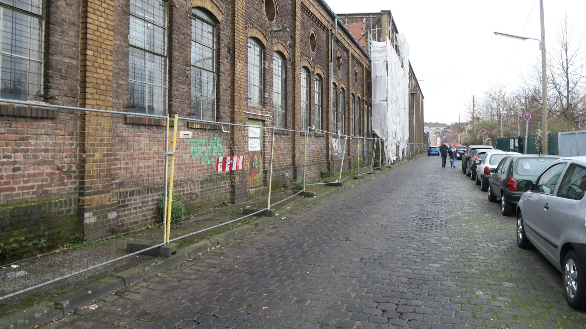 Man sieht einen Bauzaun vor einem heruntergekommenen ehemaligen Industriegebäude.