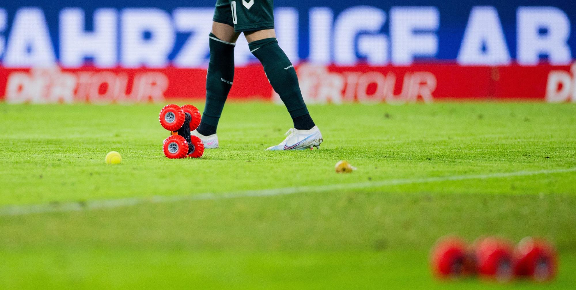 Ferngelenkte Autos fahren beim Heimspiel des 1. FC Köln gegen Werder Bremen auf dem Spielfeld im Rhein-Energie-Stadion neben Tennisbällen umher.