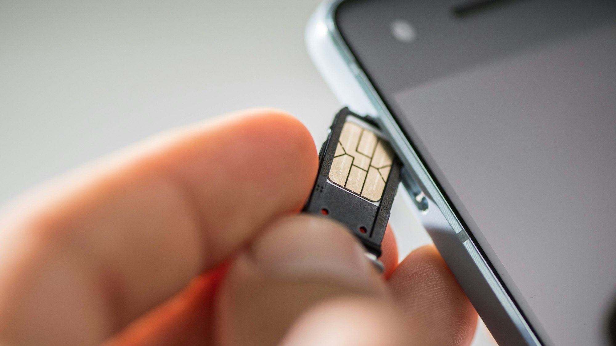 Eine Hand führt eine SIM-Karte in ein Smartphone ein.