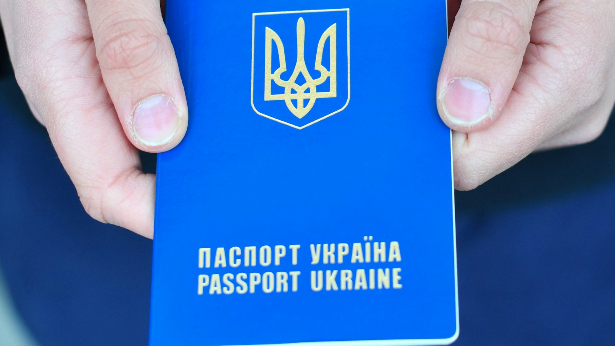 Ein Pass der Ukraine: das blaue Dokument wird von zwei Händen in die Kamera gehalten.