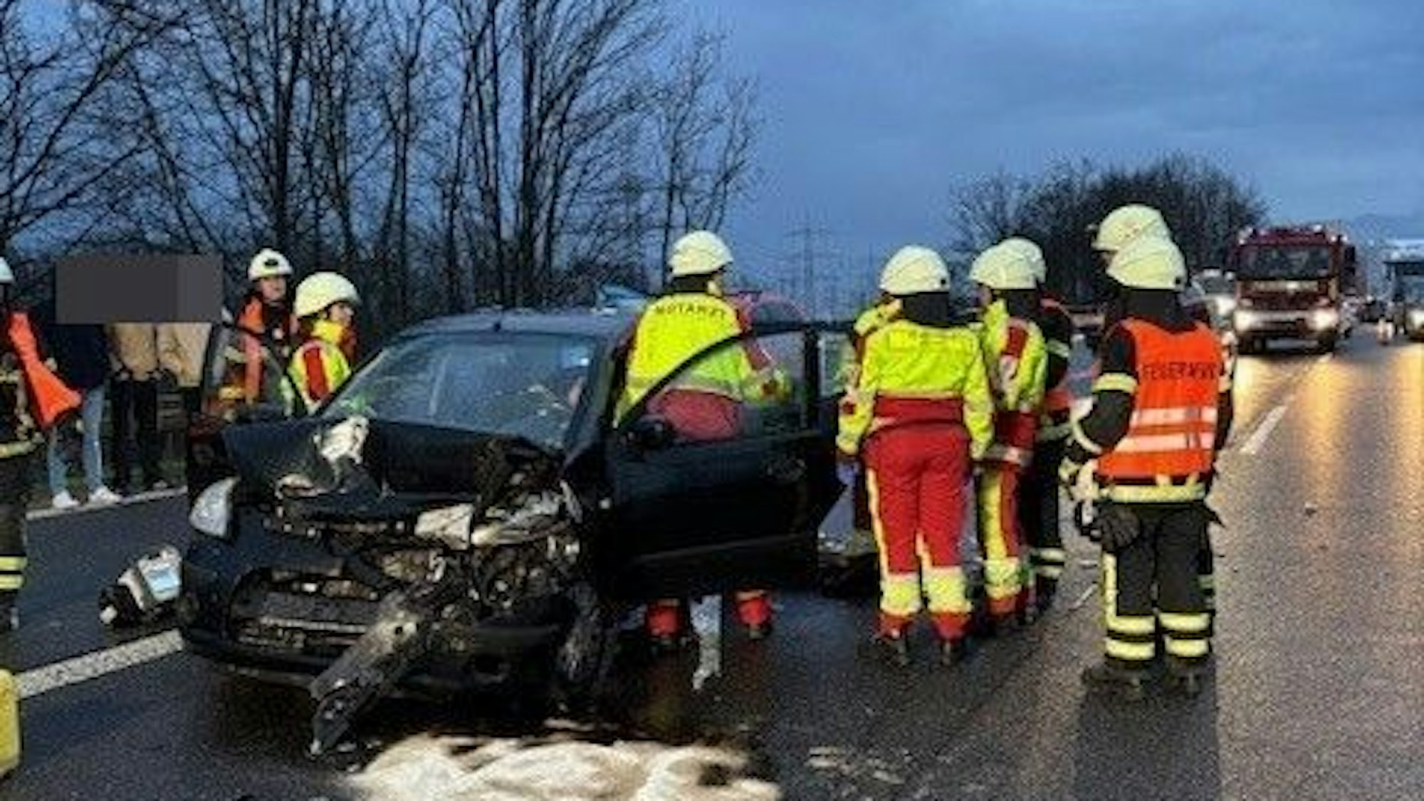 Feuerwehrleute stehen nach einem Unfall auf der A553 an einem beschädigten Auto.