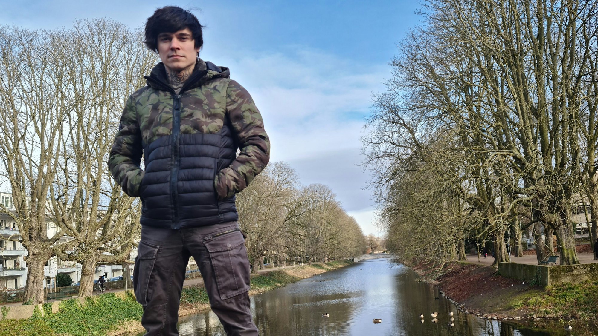 Ein junger Mann steht auf einer Beton-Brüstung, im Hintergrund ist der Lindenthaler Kanal zu sehen.