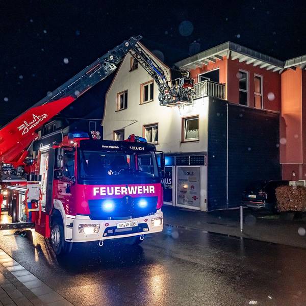 Ein Feuerwehrauto mit Drehleiter. Über diese löschen Einsatzkräfte einen Brand über einen Balkon eines Wohnhauses.