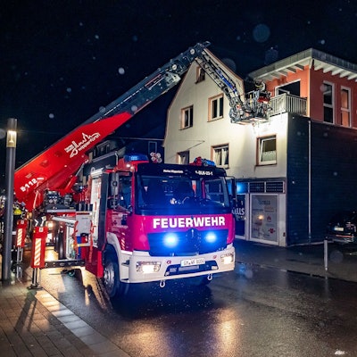 Ein Feuerwehrauto mit Drehleiter. Über diese löschen Einsatzkräfte einen Brand über einen Balkon eines Wohnhauses.