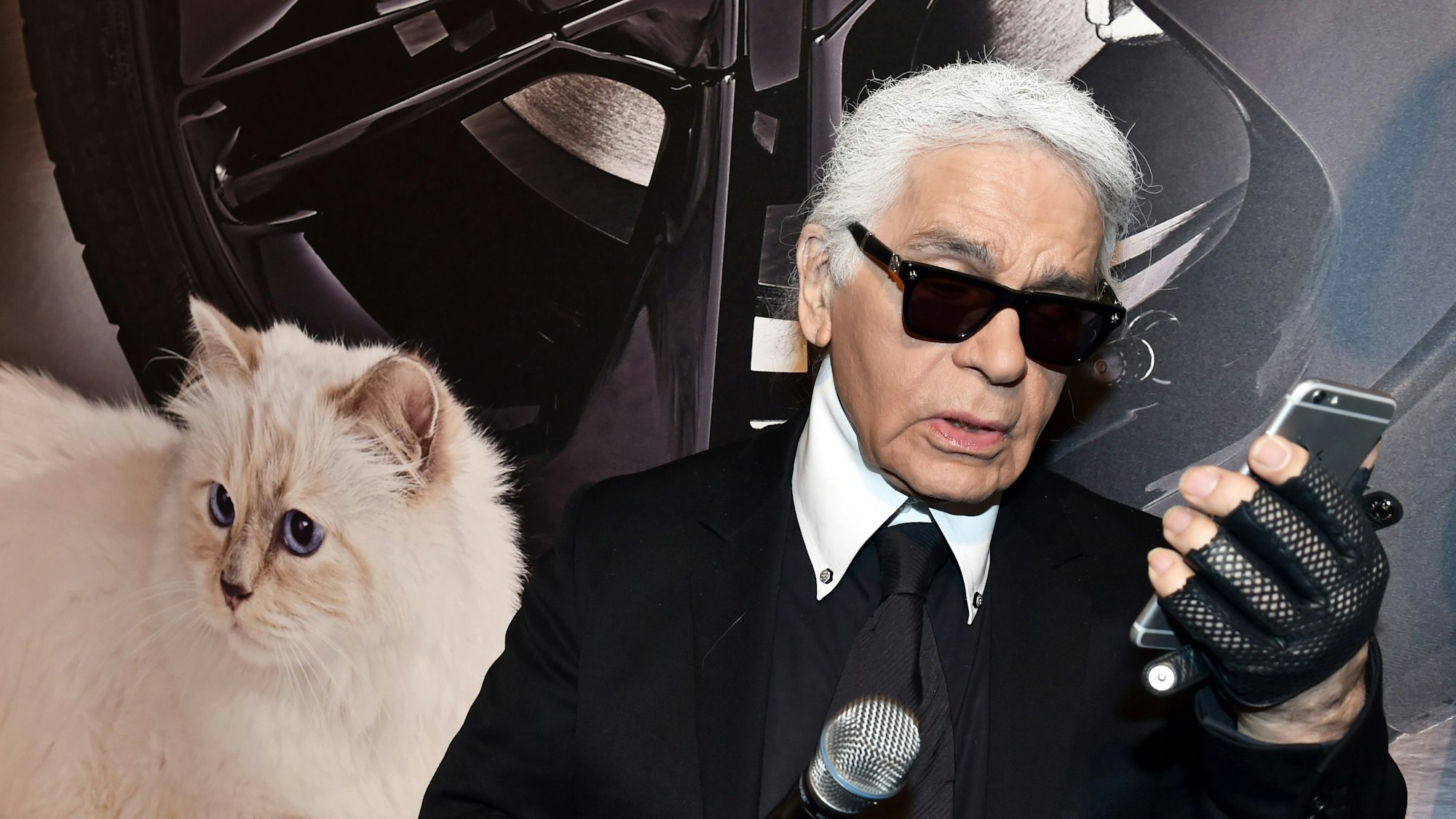 Der Modedesigner Karl Lagerfeld blickt neben einem Foto seiner Birma-Katze Choupette auf sein Smartphone.