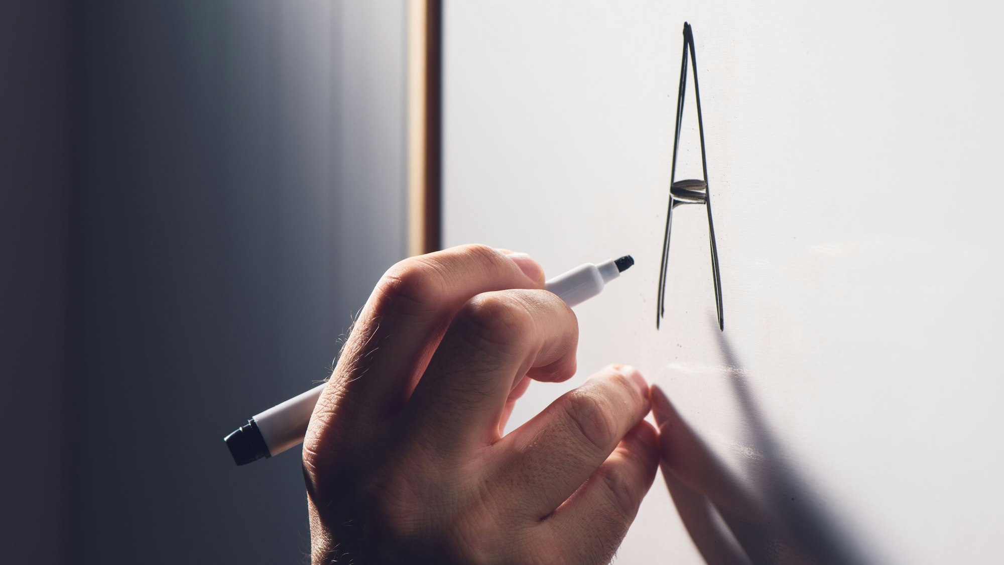 eine Hand schreibt mit einem schwarzen Stift ein A an ein Whiteboard