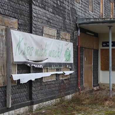 Ein Plakat mit der Aufschrift „Küss mich wach“ hängt an der Fassade des Bahnhofs Blankenheim-Wald. Der untere Teil ist bereits zerrissen.