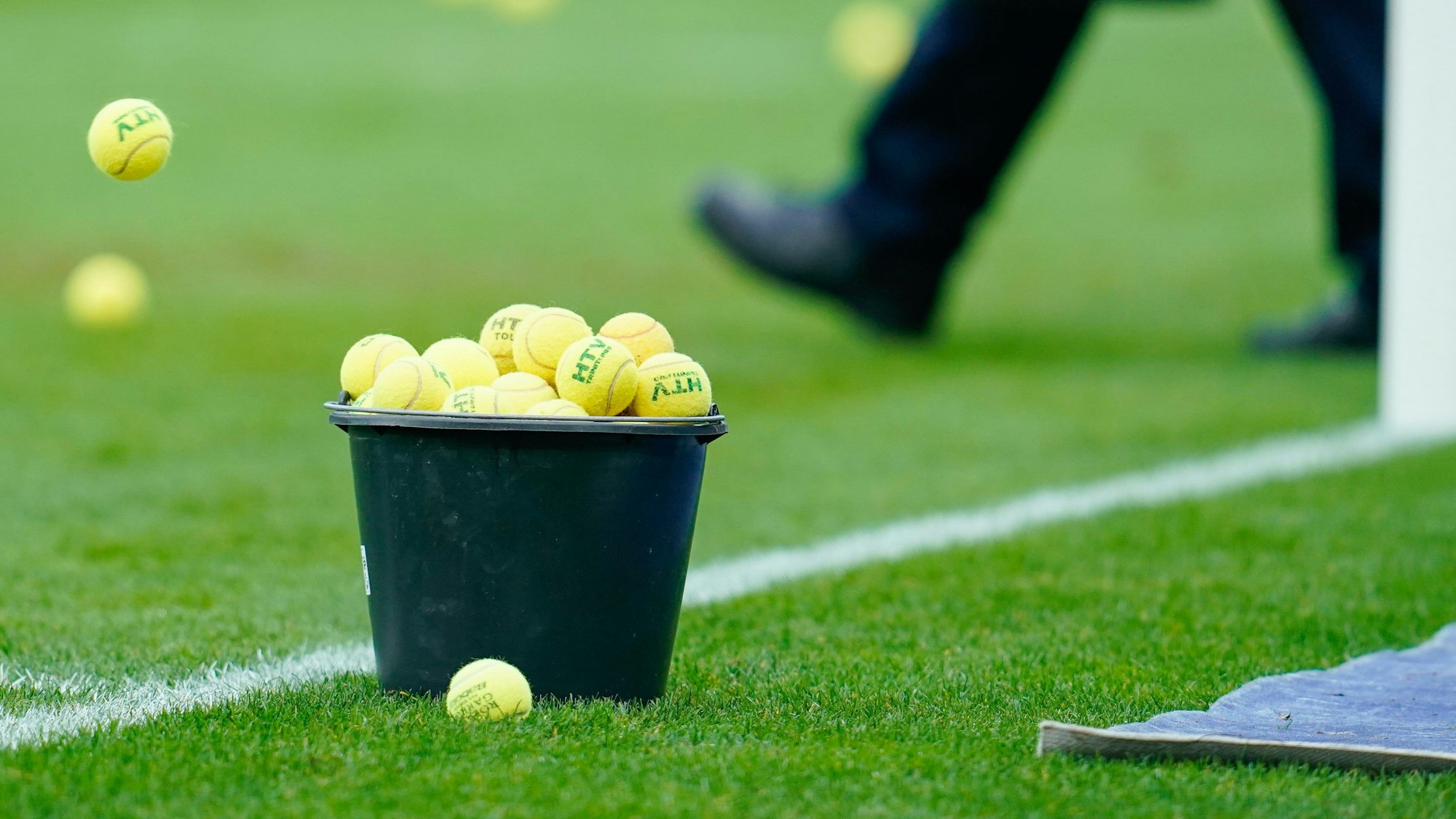 Ein Eimer mit eingesammelten Tennisbällen steht am Spielfeldrand.