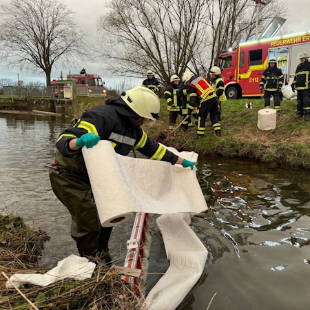 Auf dem Foto sind Feuerwehrleute zu sehen, die versuchen, den Ölfilm auf der Swist zu binden.
