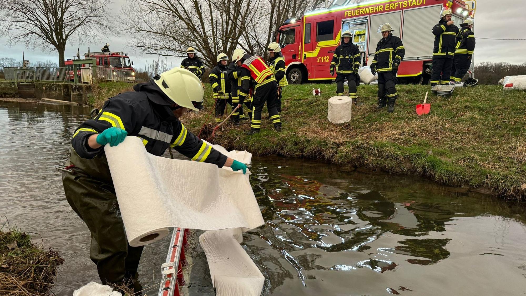 Auf dem Foto sind Feuerwehrleute zu sehen, die versuchen, den Ölfilm auf der Swist zu binden.
