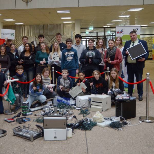Schülerinnen, Schüler, Lehrer, Lehrerinnen und Landrat Markus Ramers haben sich zu einem Gruppenbild formiert, vor ihnen ausrangierte Elektrogeräte wie Drucker und Toaster sowie Kabel und Lichterketten.
