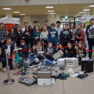 Schülerinnen, Schüler, Lehrer, Lehrerinnen und Landrat Markus Ramers haben sich zu einem Gruppenbild formiert, vor ihnen ausrangierte Elektrogeräte wie Drucker und Toaster sowie Kabel und Lichterketten.
