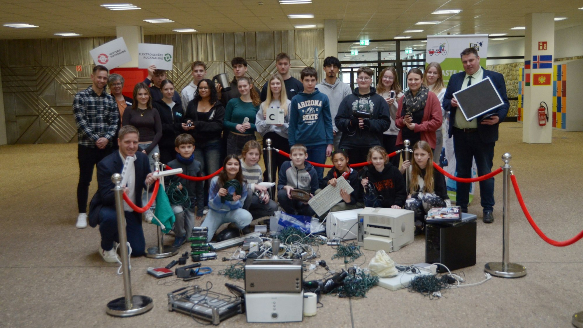 Schülerinnen, Schüler, Lehrer, Lehrerinnen und Landrat Markus Ramers haben sich zu einem Gruppenbild formiert, vor ihnen ausrangierte Elektrogeräte wie Drucker und Toaster sowie Kabel und Lichterketten.