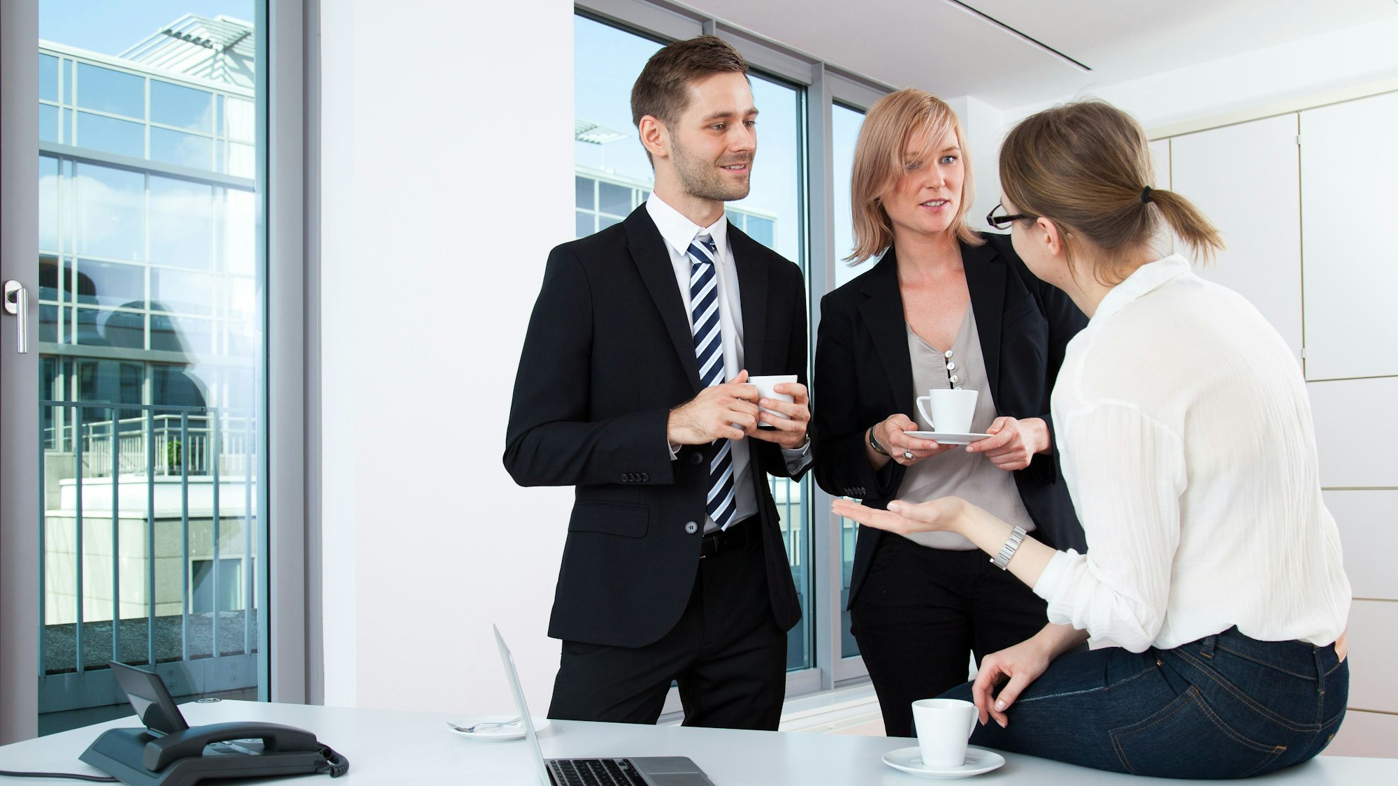 Ein Mann und zwei Frauen unterhalten sich bei einem Kaffee in einem Büro.