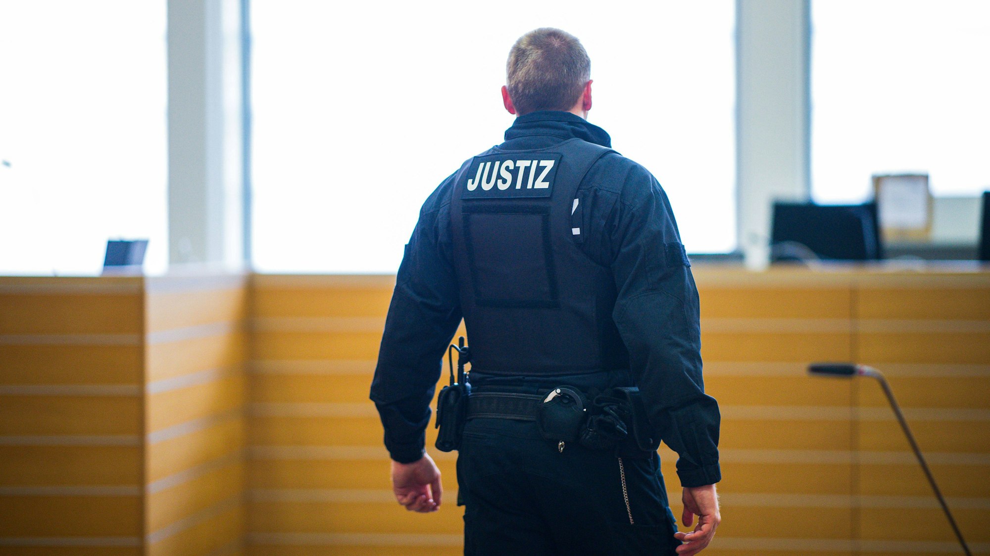 Ein Gerichtsangestellter ist von hinten zu sehen, auf seiner Uniform ist auf Schulterhöhe "Justiz" zu lesen.