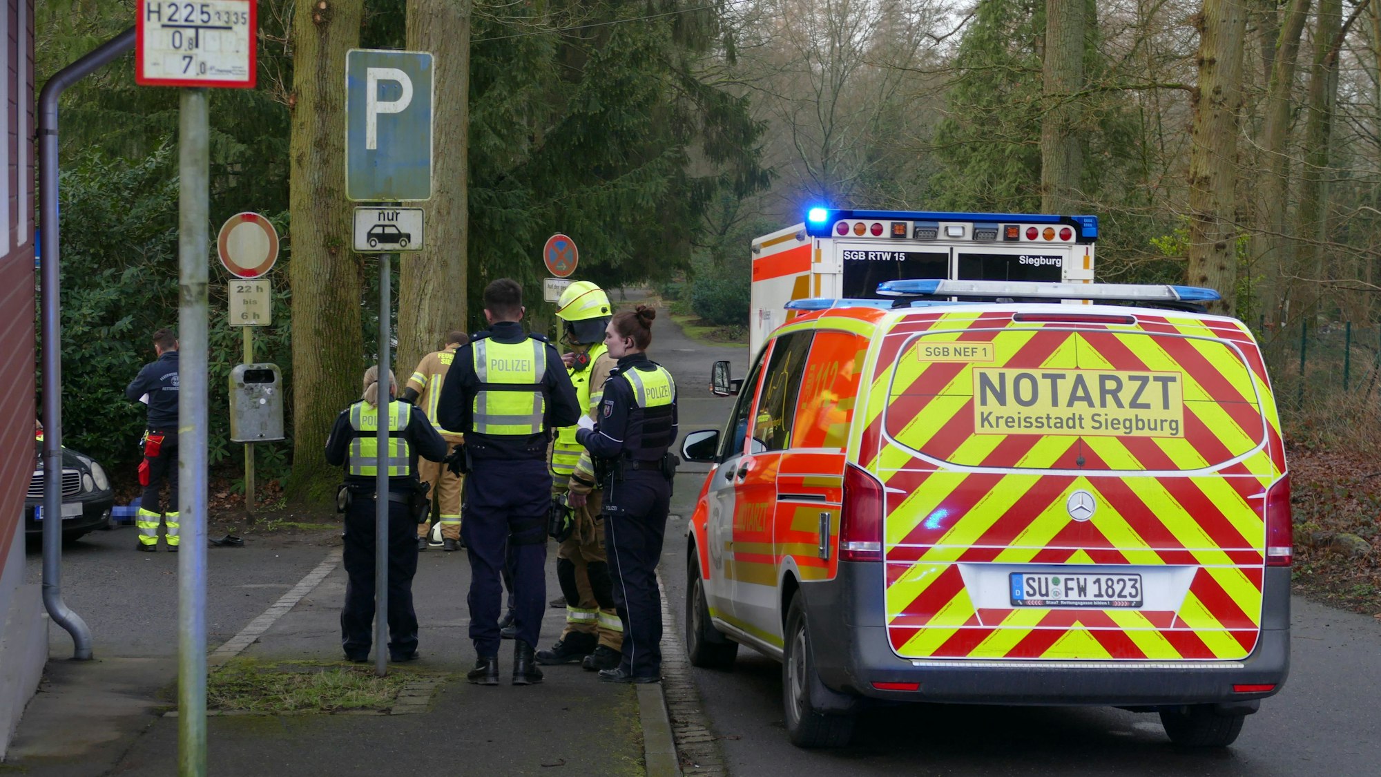 Polizsiten und Feuerwehrleute stehen neben einem Notarztfahrzeug.