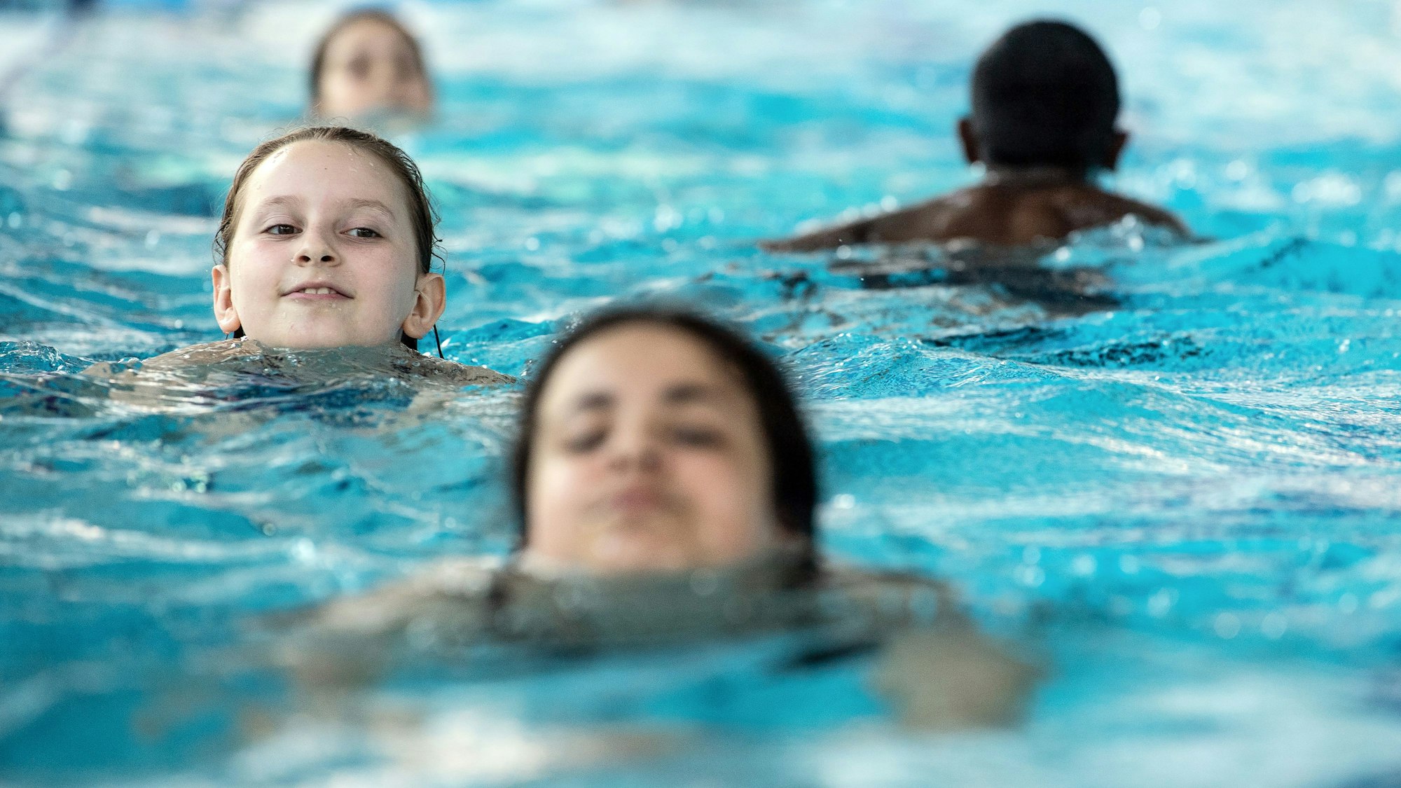 Vier Kinder schwimmen im Wasser eines Schwimmbades.