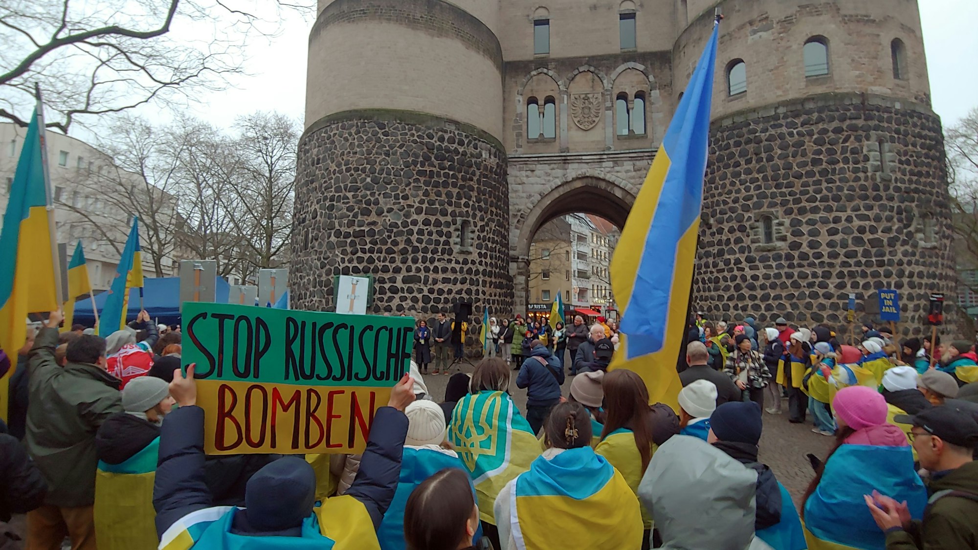 Zu sehen sind Demonstranten, die auf dem Kölner Rudolfplatz stehen und blau-gelbe Fahnen und Kleidung tragen.