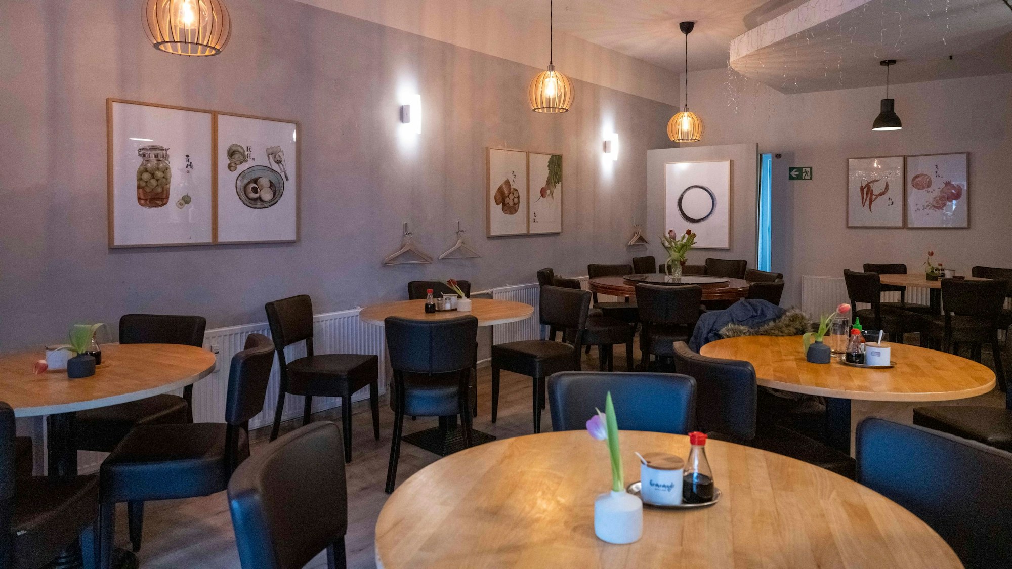 Das Restaurant Lai de Hao in Köln mit runden Tischen und dunklen Stühlen, an den Wänden hängen Bilder.