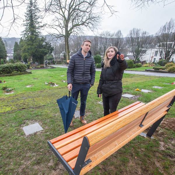 Ein Mann und eine Frau stehen vor einer Bank auf dem Friedhof.