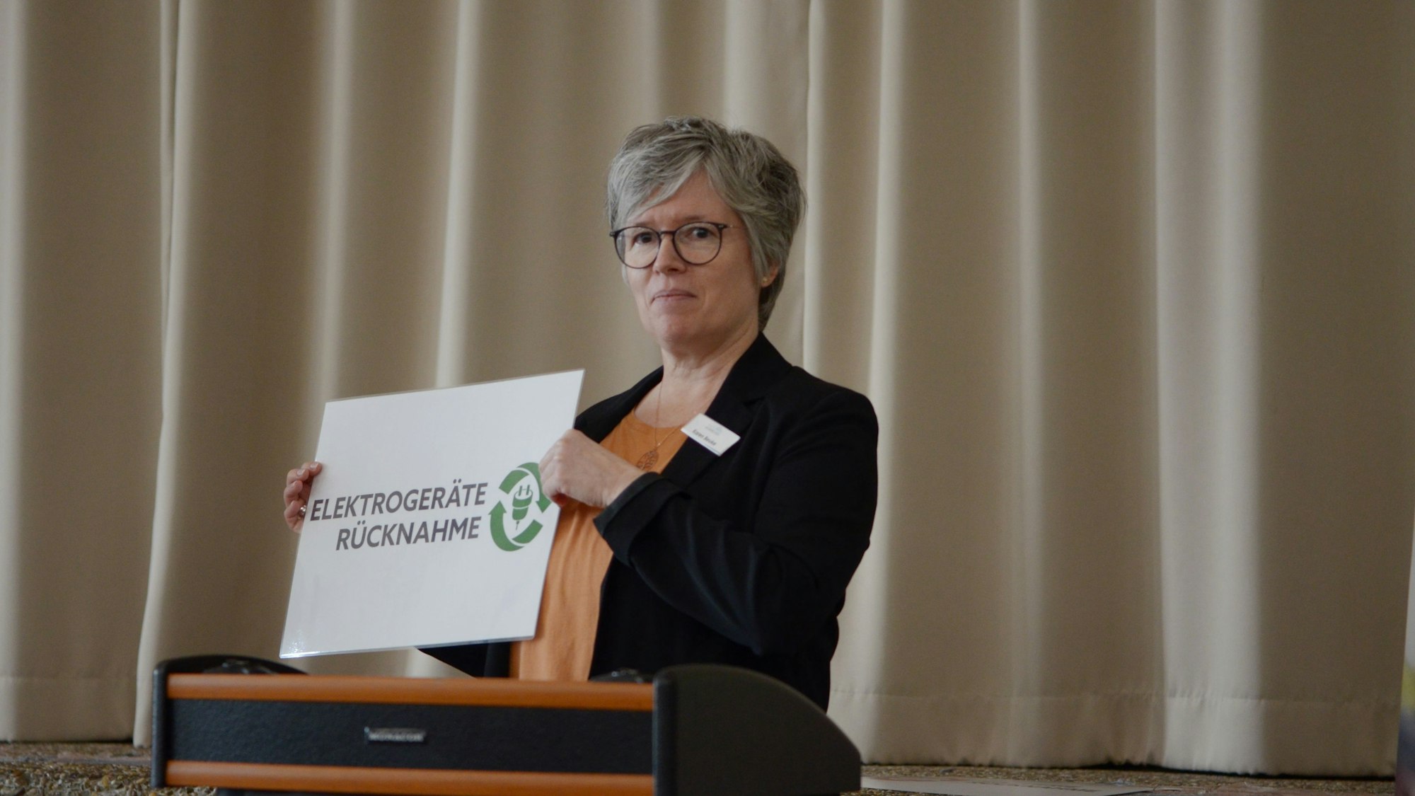 Karen Beuke hält ein Schild in der Hand mit der Aufschrift „Elektrogeräte - Rücknahme“, wie es Sammelstellen verwenden.