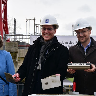 Bürgermeister und Beigeordneter halten Stein und Mörtel, sowie Zeitkapsel in der Hand.