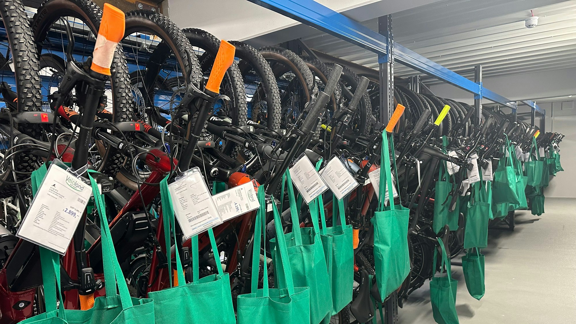 Fahrräder hängen in einem Lagerregal, bevor sie verkauft werden. Teile, die später montiert werden, hängen in Taschen am Rad.