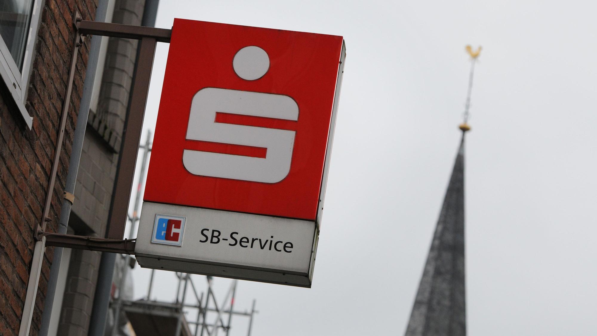 Das Logo einer Sparkasse hängt über dem Eingang einer Sparkassen-Filiale in einer Fußgängerzone (Symbolbild).