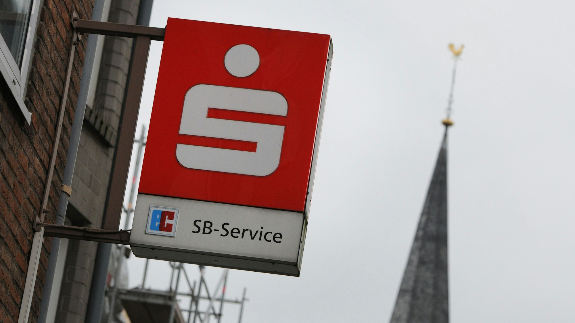 Das Logo einer Sparkasse hängt über dem Eingang einer Sparkassen-Filiale in einer Fußgängerzone (Symbolbild).