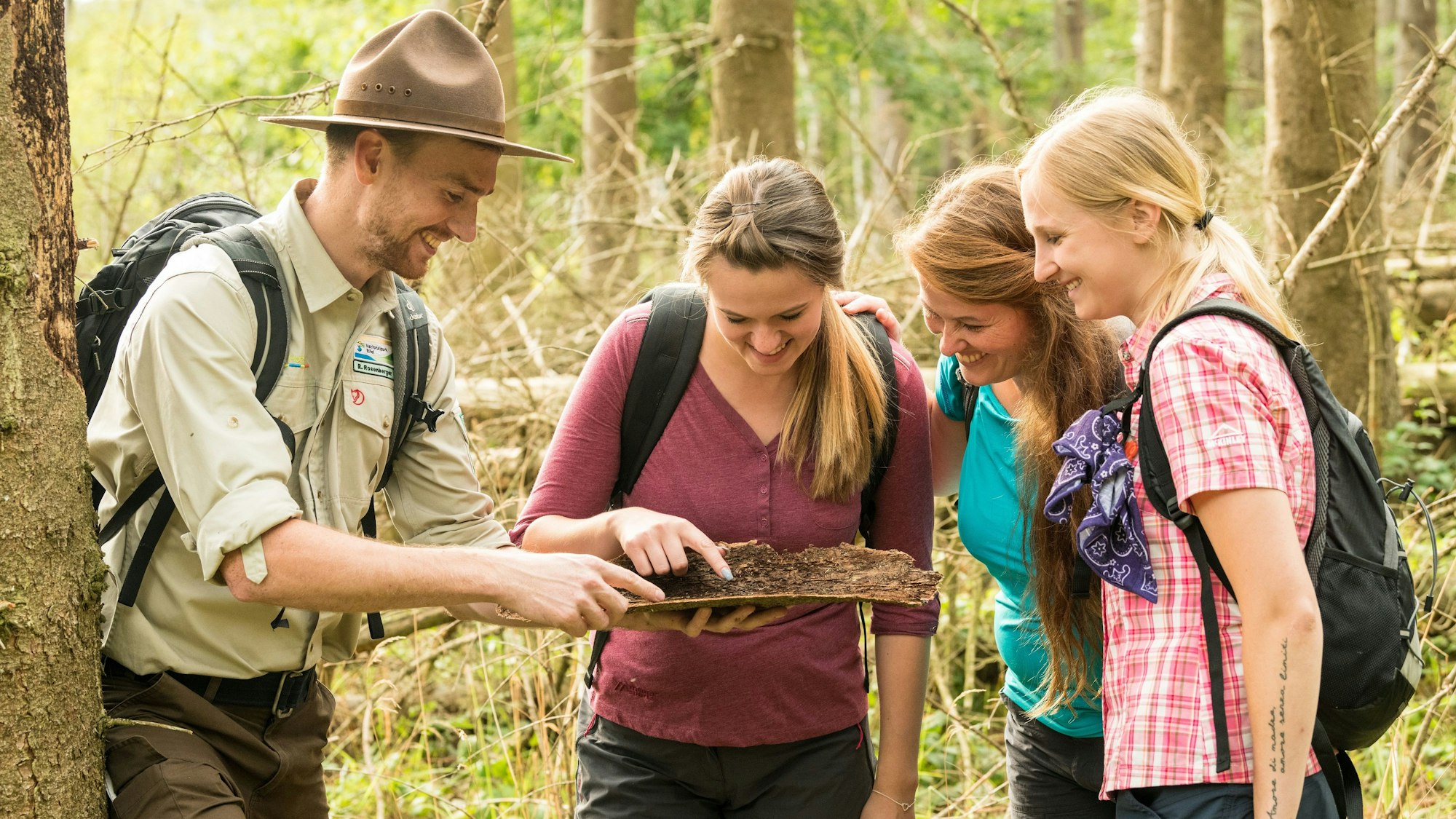 drei Wanderinnen und ein Ranger stehen im Wald und betrachten eine abgefallene Baumrinde