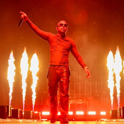 Der Rapper steht vor Flammen und hält sein Mikrofon in die Luft