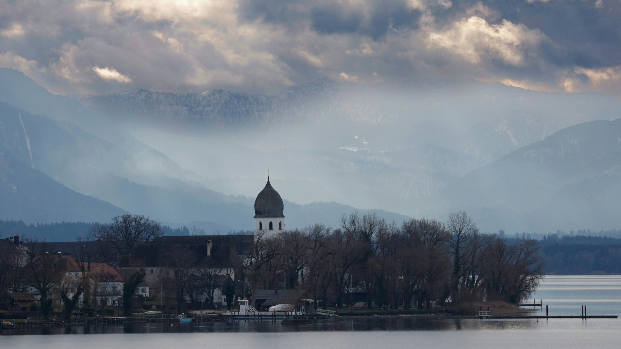 Der Glockenturm der Klosteranlage Frauenchiemsee auf der Fraueninsel im Chiemsee zeigt sich bei wechselhaftem Wetter und Temperaturen um den Gefrierpunkt vor der Kulisse der Chiemgauer Berge. (Archivbild)