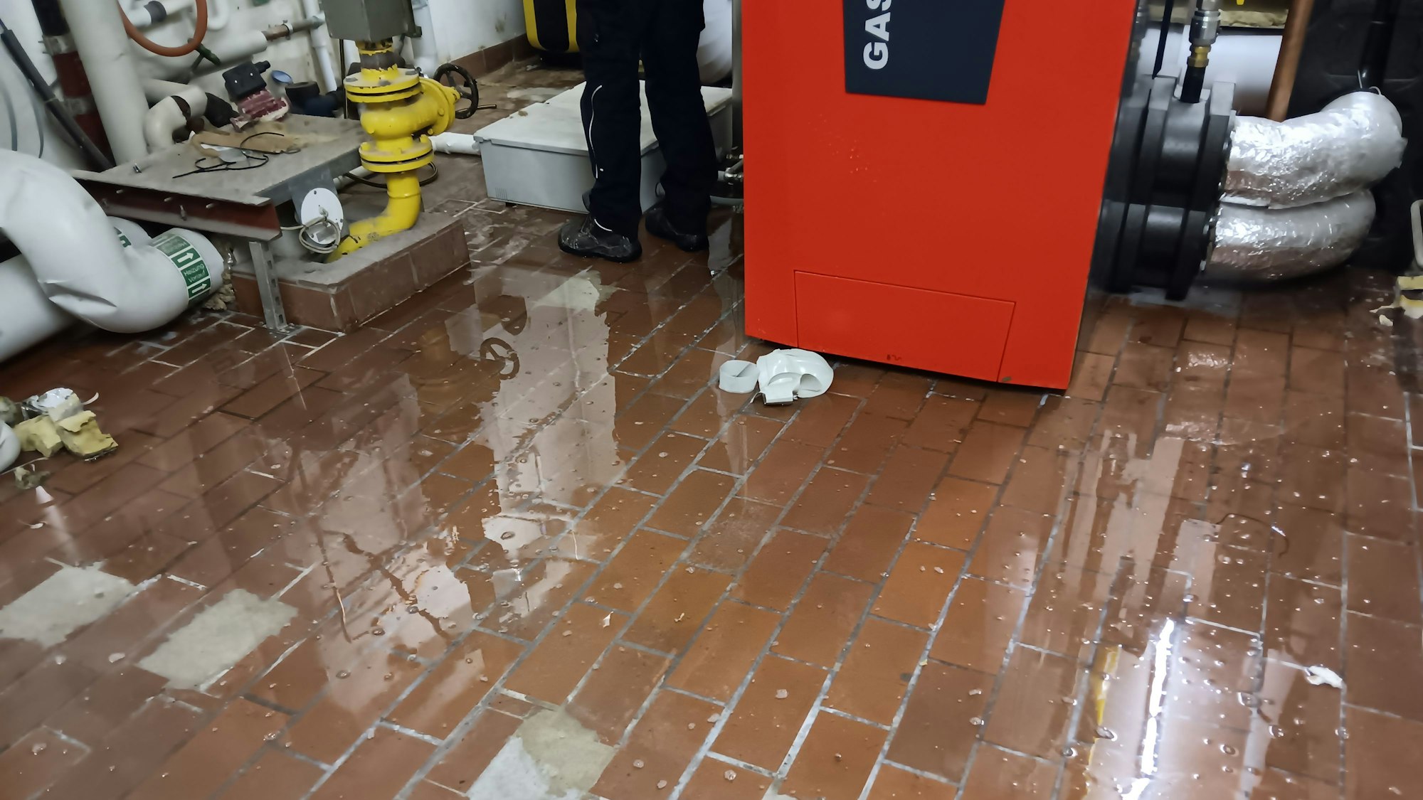 Ein Heizungsraum mit vielen Rohren. Auf dem Boden ist ein Wasserfilm zu sehen.