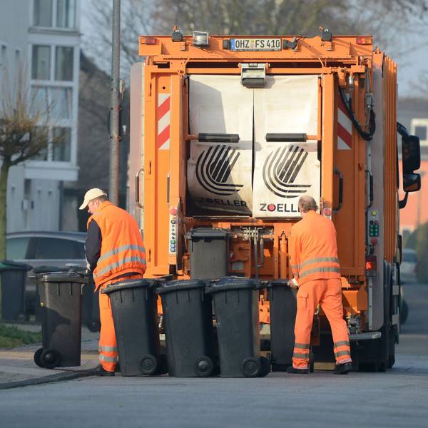 Zwei Männer von der Müllabfuhr entleeren Restmülltonnen.