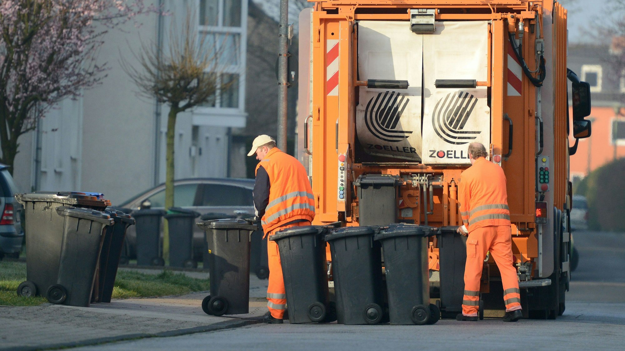 Zwei Männer von der Müllabfuhr entleeren Restmülltonnen.