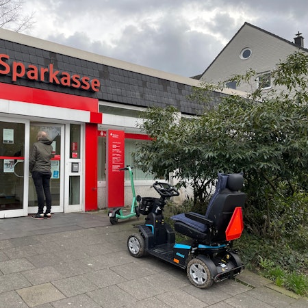 Ein Mann steht vor der Glastür einer kleinen Sparkassen-Filiale.