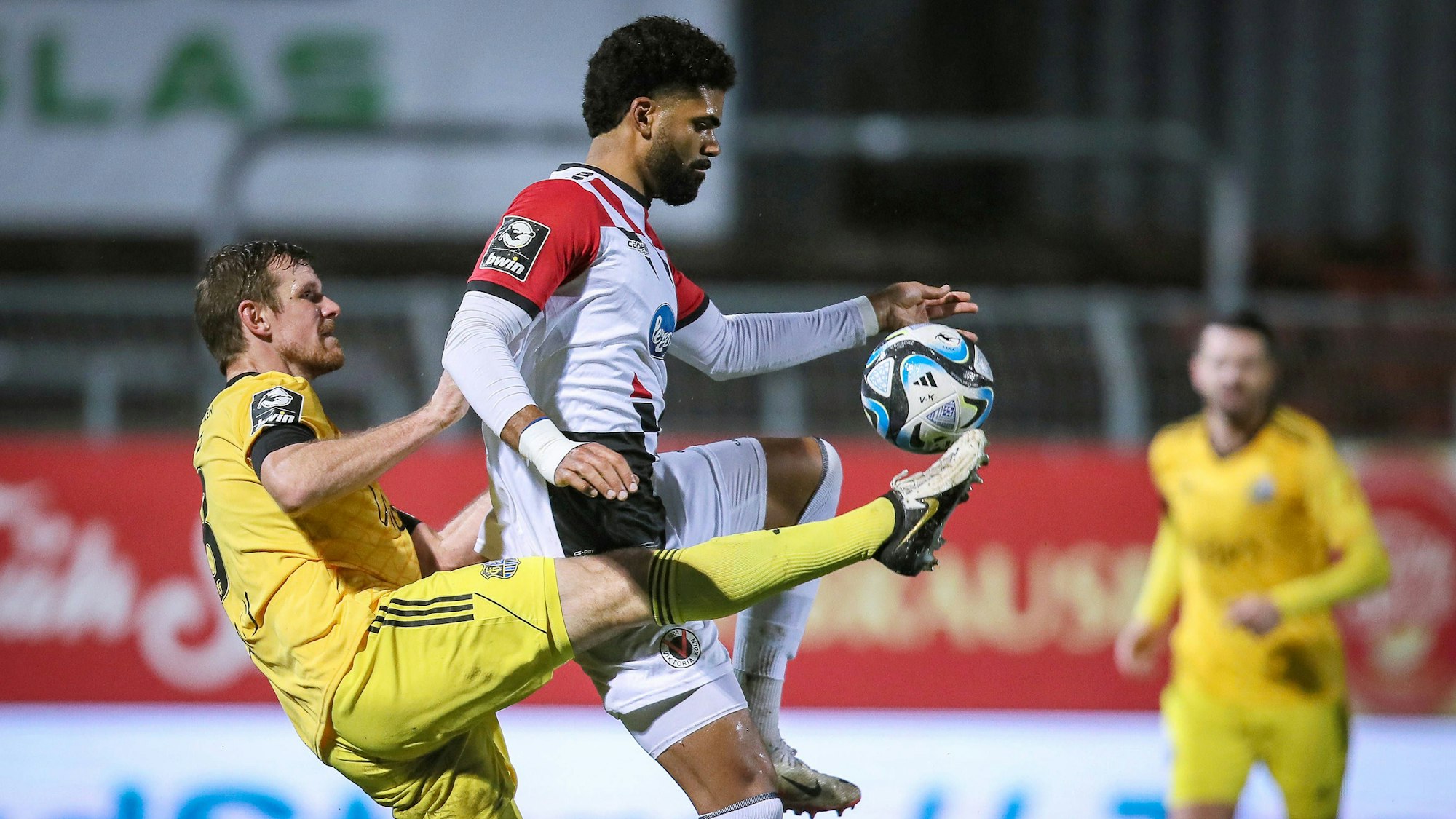 Ein Fußballspieler tritt in Richtung des Balls, der kurz davor ist, von dem Oberschenkel eines anderen Spielers aufgenommen zu werden.