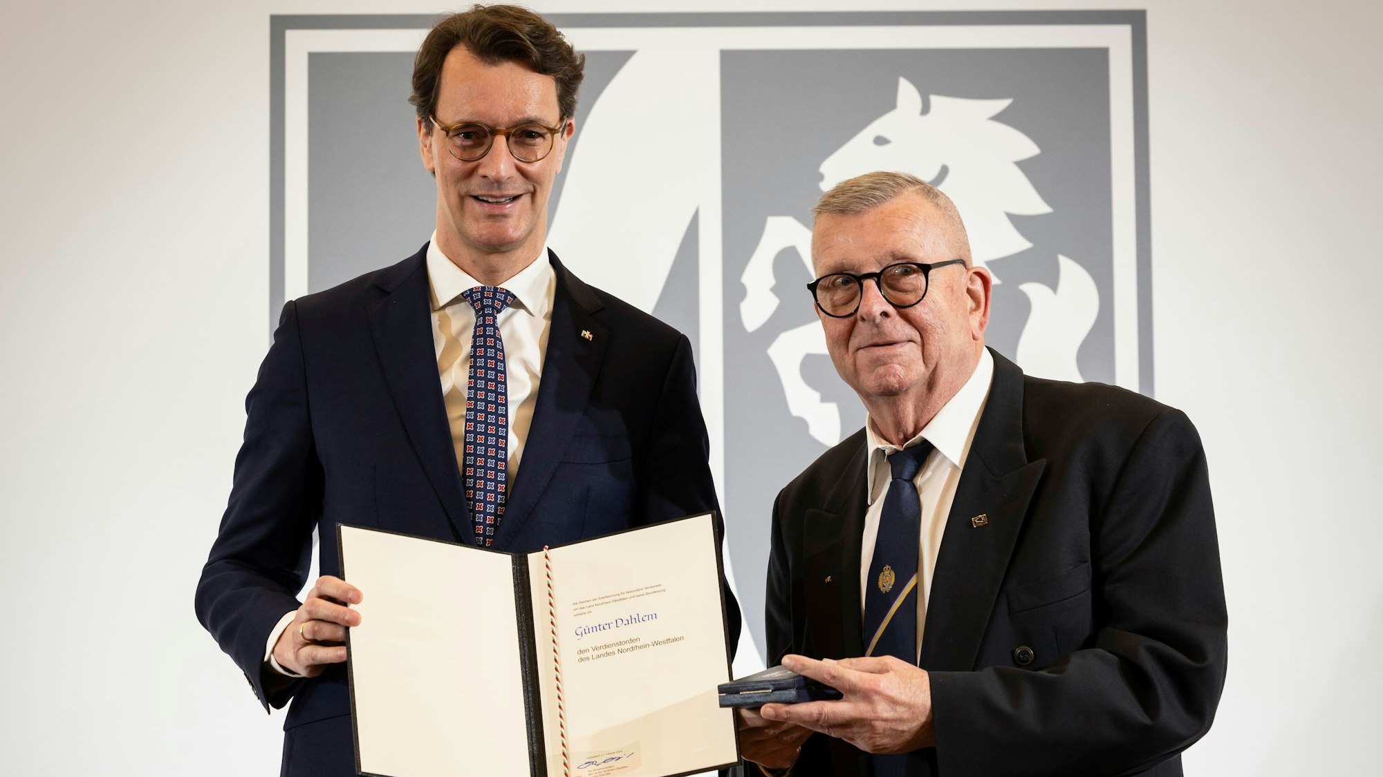 Ministerpräsident Hendrik Wüst hält eine Urkunde in der Hand, Günter Dahlem aus Euskirchen den Landesverdienstorden.