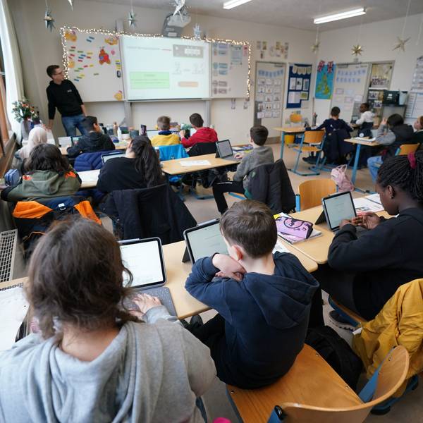 Kinder sitzen in einem vollen Klassenraum vor ihren Tablets.