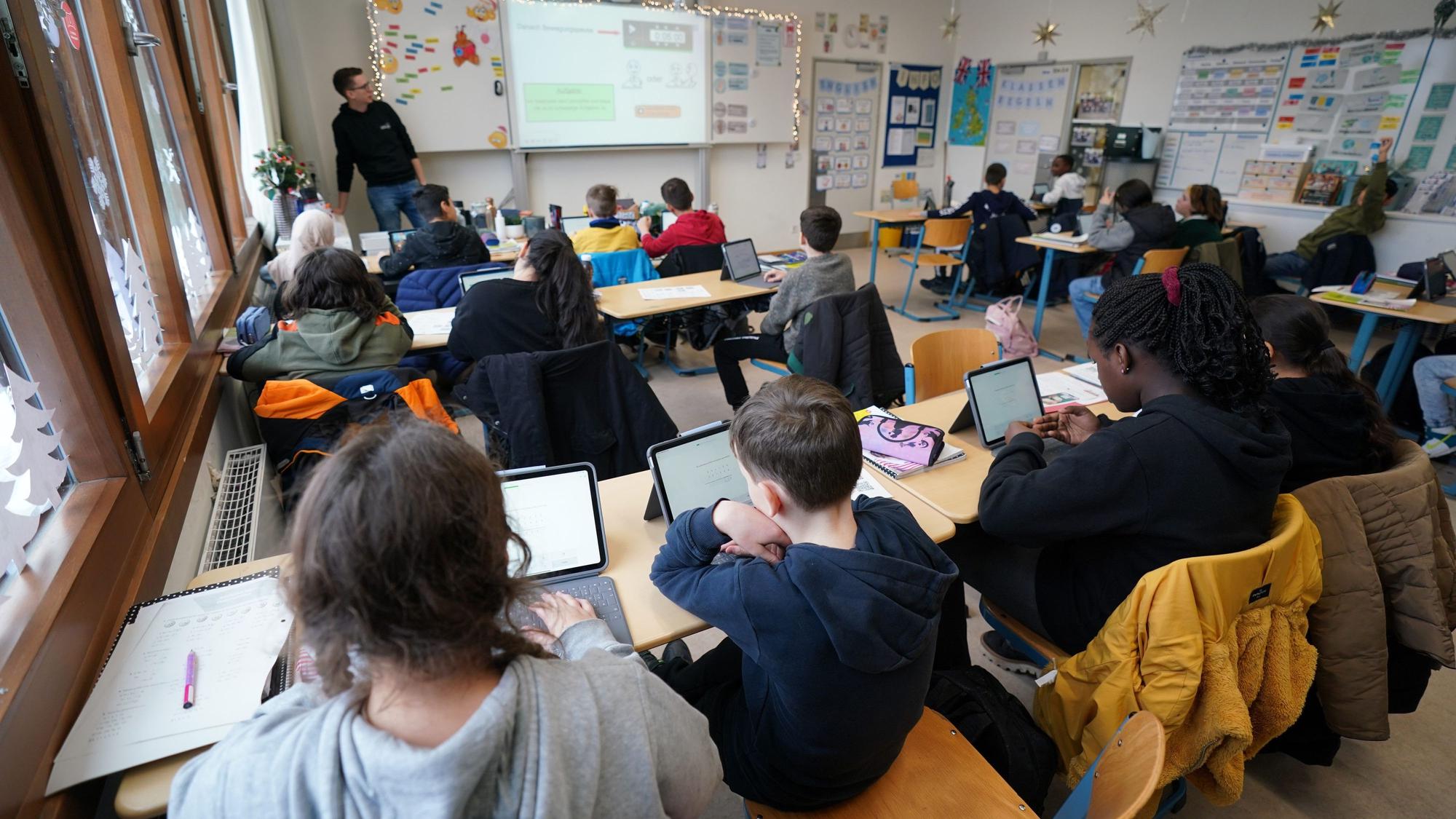 Kinder sitzen in einem vollen Klassenraum vor ihren Tablets.