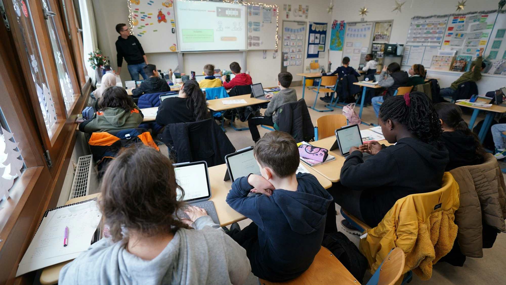 Kinder sitzen in einem vollen Klassenraum vor ihren Tablets.