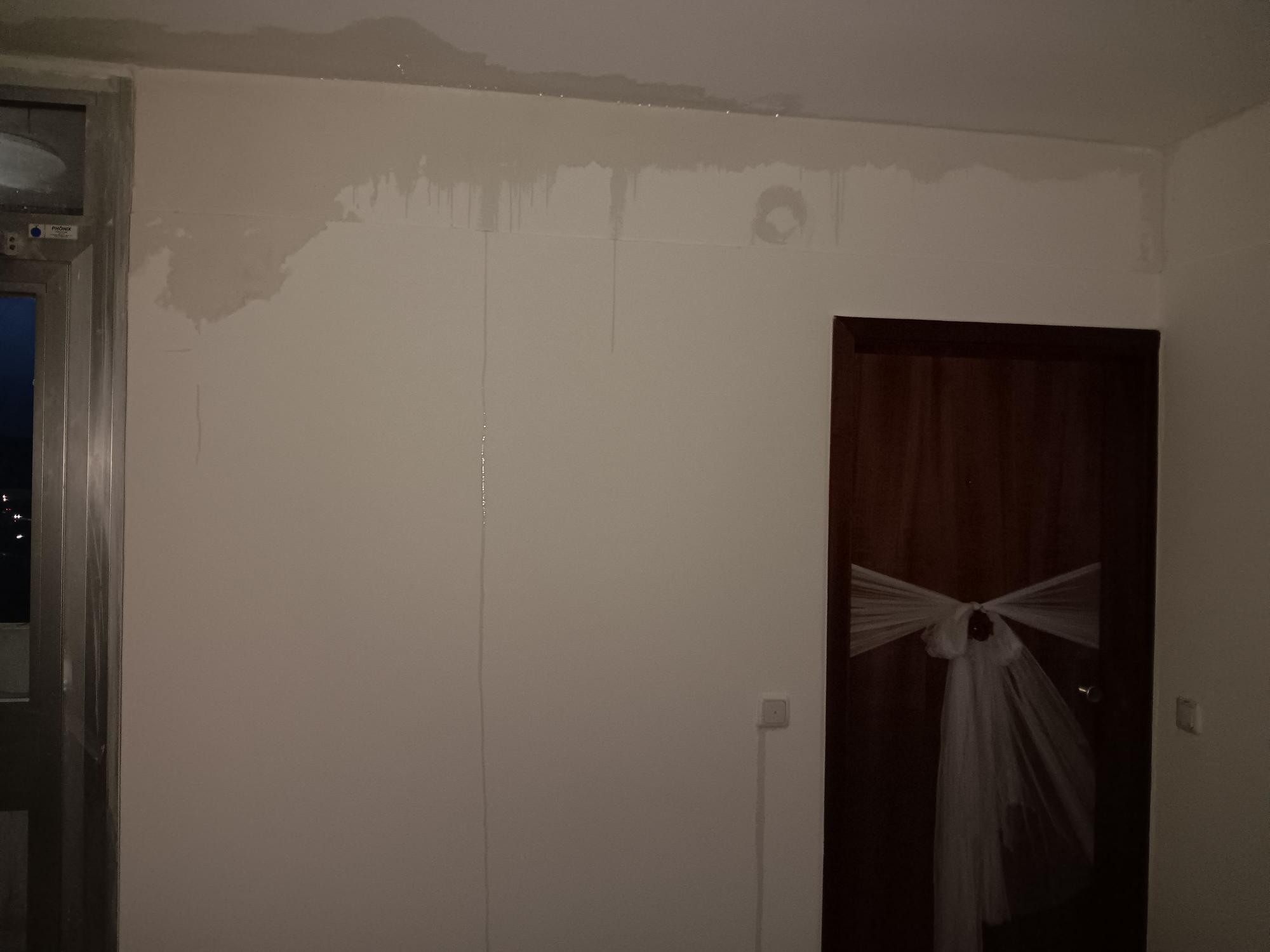 In einem Hausflur verdunkeln Wasserflecke die weiße Wand. An einigen Stellen fließt das Wasser die Wand hinunter.