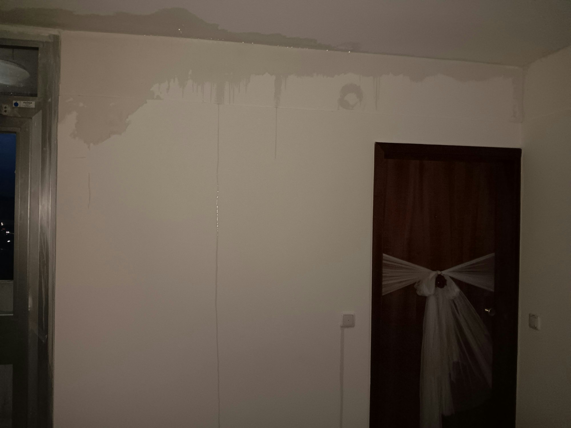 In einem Hausflur verdunkeln Wasserflecke die weiße Wand. An einigen Stellen fließt das Wasser die Wand hinunter.